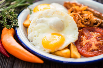 Typial breakfast with eggs, tomato, onion rings and sausage on plate