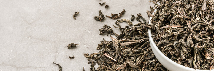 Dried tea is poured into a white ceramic cup on a gray textured background.