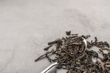 Dried tea and a spoon on a gray textured background.