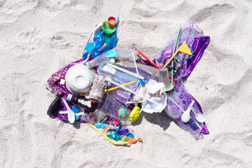 Ocean trash in fish shape laying on sand bech plastic pollution concept