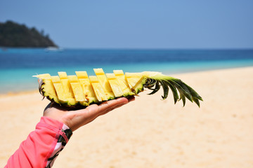 fresh pine apple slice on hand with the beach and island in background for summer concept
