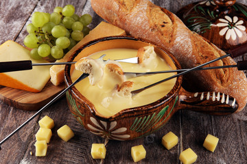 Gourmet Swiss fondue dinner on a winter evening with assorted cheeses on a board alongside a heated pot of cheese fondue with two forks dipping