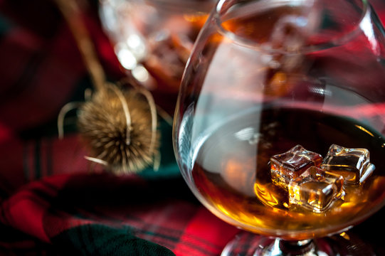 Glass of scottish whisly on a table with traditional tartan and a thisly, symbol of scotland