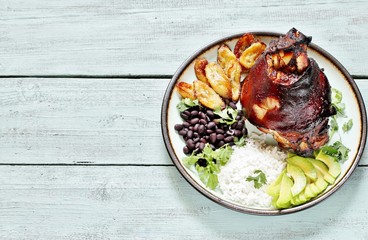 buddha bowl in latin american style. Colombian traditional food. pork knuckle ham baked, rice, black beans, fried bananas, avocado, cilantro. copy space. top view.