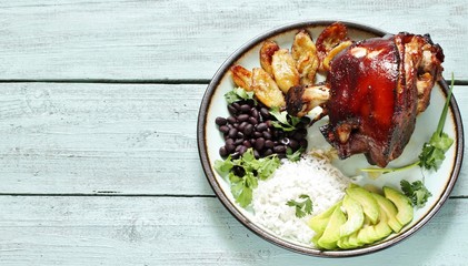 buddha bowl in latin american style. Colombian traditional food. pork knuckle ham baked, rice, black beans, fried bananas, avocado, cilantro. copy space. top view.