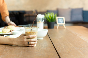 Holding glass of iced latte coffee with food on table at lunch time.