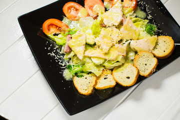 Caesar salad with bacon and quail eggs Black plate on a white wooden