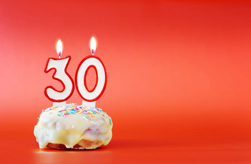 Thirty years birthday. Cupcake with white burning candle in the form of number 30. Vivid red...
