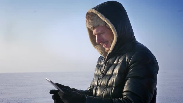 Businessman in warm coat and hood standing on frozen lake demonstrating green screen of tablet recommending the app.