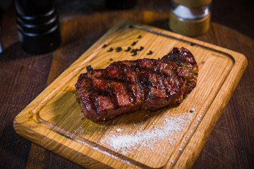 Grilled pork rib chop steak in a clay plate with oil, mustard, salt and rosemary is an old wooden table.