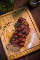 Grilled pork rib chop steak in a clay plate with oil, mustard, salt and rosemary is an old wooden table.