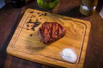 Grilled pork rib chop steak in a clay plate with oil, mustard, salt and rosemary is an old wooden table.