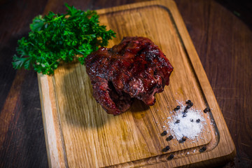 Grilled pork rib chop steak in a clay plate with oil, mustard, salt and rosemary is an old wooden table.