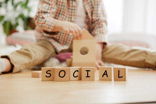 Wooden cubes with word SOCIAL in hands of little boy at home. Conceptual image about child rights, education, childhood and social problems.