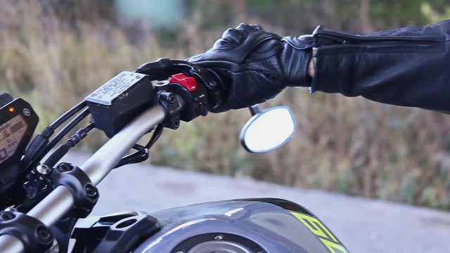 Closeup of a biker's hand. Biker twists the Handle of the Gas on the Wheel of the Motorcycle. A Biker start a motorcycle