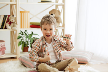 Wooden cubes with word HAPPY in hands of happy smiling little boy at home. Conceptual image about child rights, education, childhood and social problems.