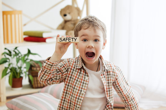 Wooden cubes with word safety in hands of happy smiling little boy at home. Conceptual image about child rights, education, childhood and social problems.