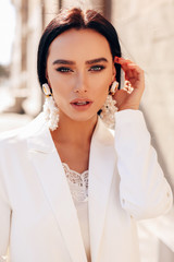 beautiful woman with dark hair in elegant white suit and accessories walking by the spring city