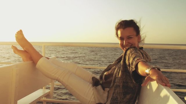Happy young woman smiling pointing at sunrise on travel at sea. On a cruise ship vacation ferry looking at camera.