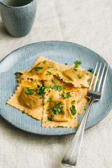 Homemade Italian ravioli pasta with parsley on a blue ceramic plate.