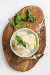 Top view of homemade vegan ice cream in a bowl is made from frozen mango and coconut milk served by fresh mint and flakes on a wooden textured board.
