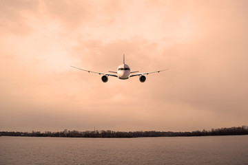 Airliner over the river dark in the city in the evening. Transport, travel.