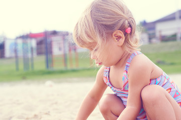 Little blonde baby girl playing with sand on the beach using plastic toys.