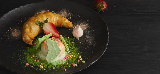 Slice of apple strudel with a scoop of vanilla ice cream on a black plate, on a wooden black table, decorated with meringue and strawberries. close-up. horizontal view of baked dessert.