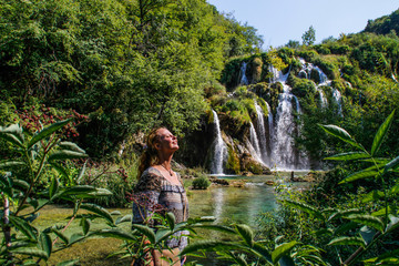 Young white female tourist smiling looking at the sun on the background of the beautiful Plitvice complex waterfall in Croatia