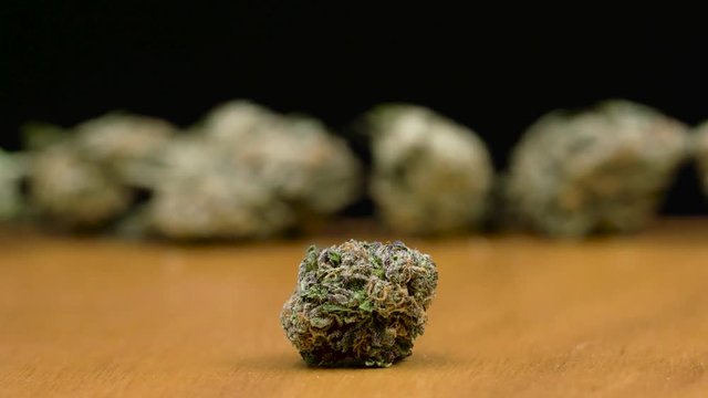 Dolly in to a beautiful cannabis bud, over a wooden table, black background.