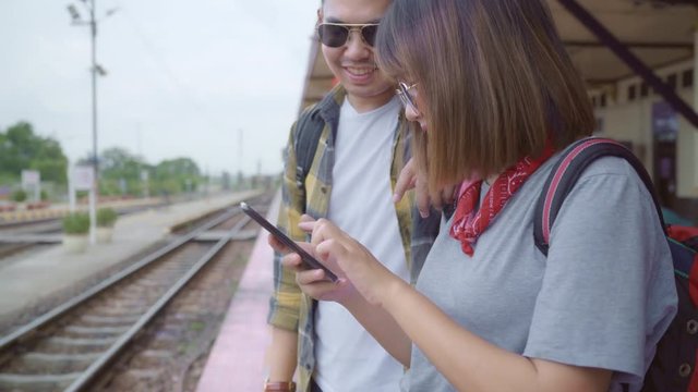 Asian backpack couple at train station, Young sweet couple tourist backpacker using mobile phone looking and direction maps on their journey in Thailand. Lifestyles couple relax and travel concept.