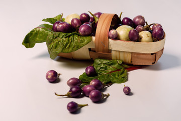 Ripe pass eggplants in a basket with beet leaves on a white background.