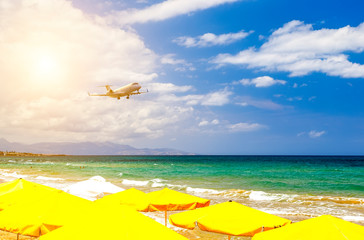Fototapeta na wymiar private business plane on landing flies over sandy beach with sun loungers on background of sunset, sun and clouds. Crete, Europe