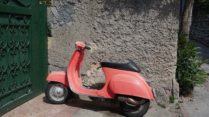 Old vintage red vespa next to a house door gate