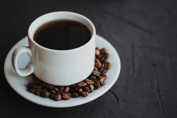 White cup of coffee and coffee beans on a dark background