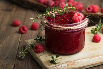 Raspberry jam in a glass jar and fresh raspberry and thyme