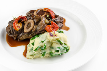Braised beef on the bone with dried tomatoes and mashed potatoes with spinach and feta cheese on a plate on a white background