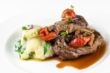 Braised beef on the bone with dried tomatoes and mashed potatoes with spinach and feta cheese on a plate on a white background