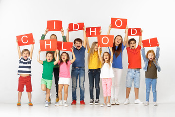 Childhood is so sweet time of life. Group of happy screaming children or teenagers with a red banners isolated in white studio background. Education and advertising concept, social rights.