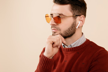 Awesome bearded young man wearing yellow sunglasses and bluetooth white earphones over beige...