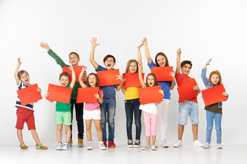 Obraz premium Group of happy screaming children with a red empty banners isolated in white studio background. Education and advertising concept