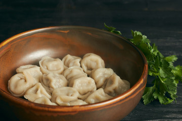 pelmeni with butter and greens on a black wooden table. Russian traditional dish of dough and minced meat. close up photo. horizontal view of the dish.