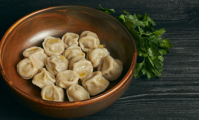 pelmeni with butter and greens on a black wooden table. Russian traditional dish of dough and minced meat. close up photo. horizontal view of the dish.