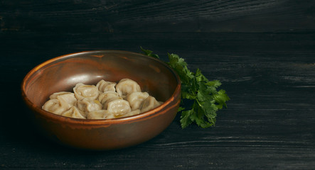 pelmeni with butter and greens on a black wooden table. Russian traditional dish of dough and minced meat. close up photo. horizontal view of the dish. copy space.