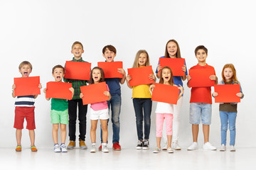 Fototapeta premium Group of happy screaming children with a red empty banners isolated in white studio background. Education and advertising concept