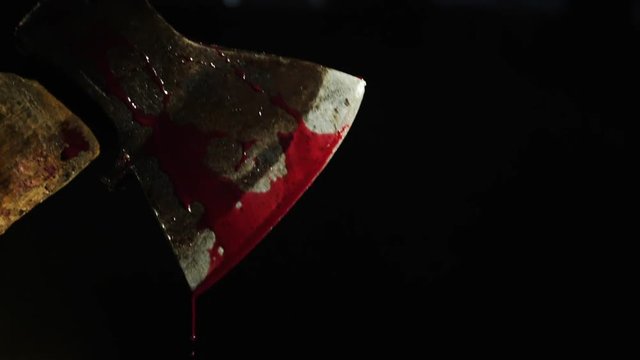 Axe with blood in hand on the dark background. Close-up shot