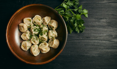 pelmeni with butter and greens on a black wooden table. Russian traditional dish of dough and minced meat. close up photo. horizontal view of the dish. copy space. view from above