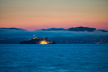 Naklejka premium Alcatraz Island at sunset surrounded by fog and mountains