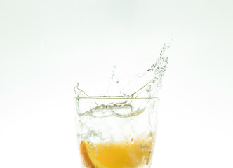 Slice the orange slice in a glass of water and make a spray on a white background. water spray in the air. a slice of citrus drops in a glass spray.