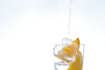 ice drink with orange and ice in the studio on a white background. a stream of water pours into the glass.